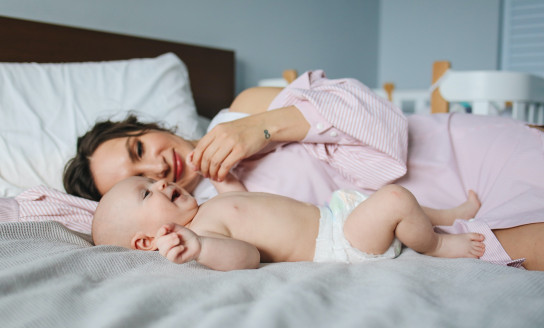 woman in pink dress lying on bed next to baby in diapers 3875130