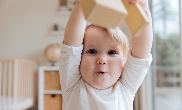 baby in white onesie holding wooden blocks 3933250